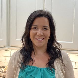 Smiling woman in a kitchen wearing a teal top and beige cardigan.