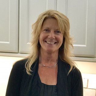 Smiling blonde person standing in a kitchen with white cabinets and warm under-cabinet lighting