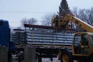 Yellow excavator loading metal beams onto a truck outdoors in a cloudy industrial yard