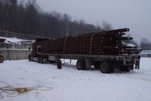 Flatbed truck loaded with long metal beams in a snowy industrial yard