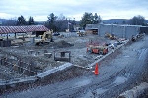 Snowy construction site with excavators, equipment, and an unfinished building under overcast skies
