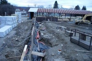 Construction site with excavated trench, concrete forms, and a shed in the background