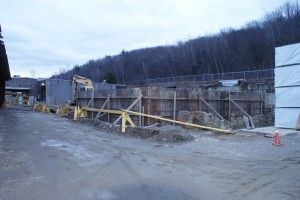 Construction site with wooden fencing, gravel road, and forested hillside in the background