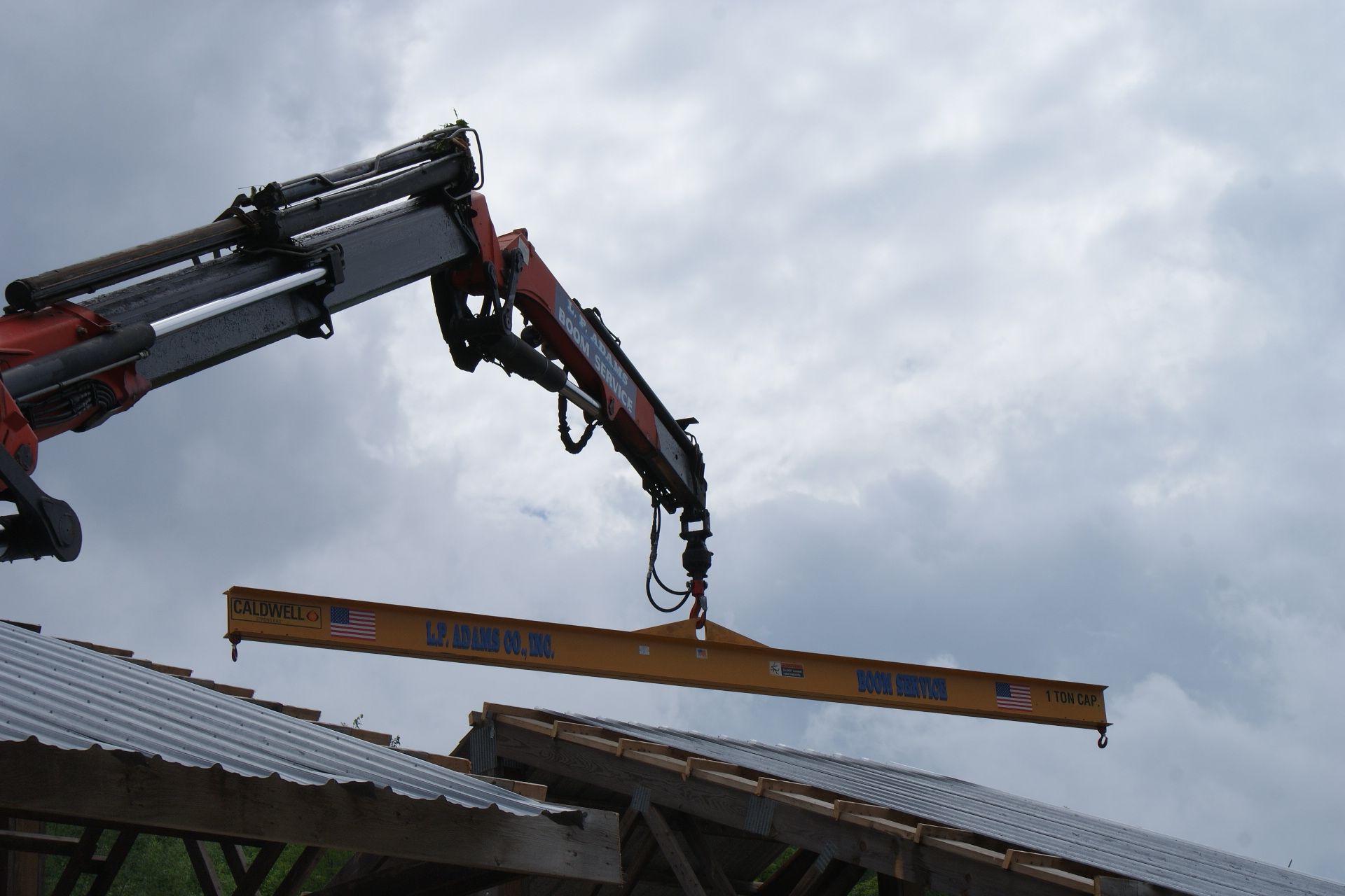 Crane lifting a long beam over a roof under a cloudy sky