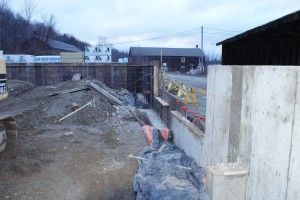 Construction site with excavated ground, gravel pile, and a concrete wall beside a building under overcast sky