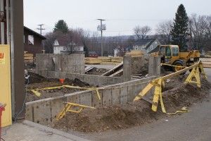 Construction site with yellow excavator, concrete walls, and caution tape around a trench
