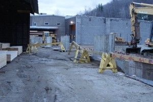 Construction site with concrete barriers and a parked excavator on a muddy, fenced roadway