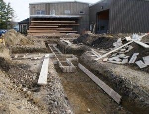 Construction site with dug trench, wooden forms, and building exterior in the background