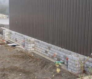 Brick foundation along a brown metal-sided building with exposed ground and a small pipe/utility connection.