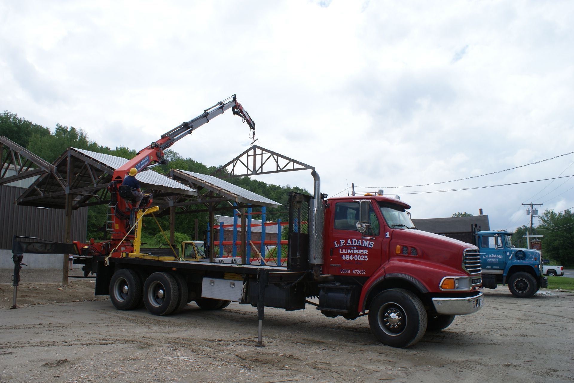 Red cargo truck with crane lifting green metal truss in an outdoor yard