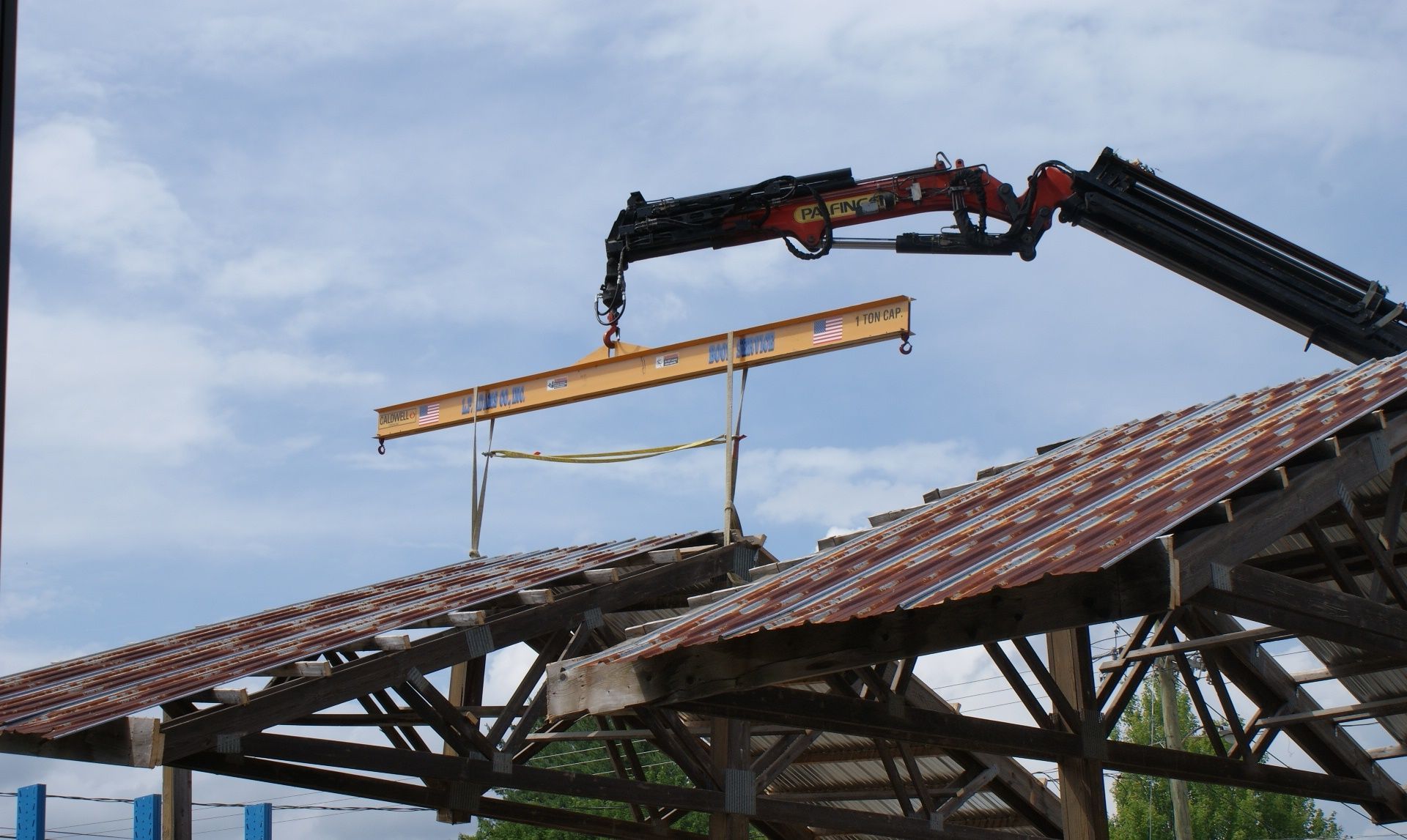 Crane lifting roof panels on a partially demolished building under a cloudy sky