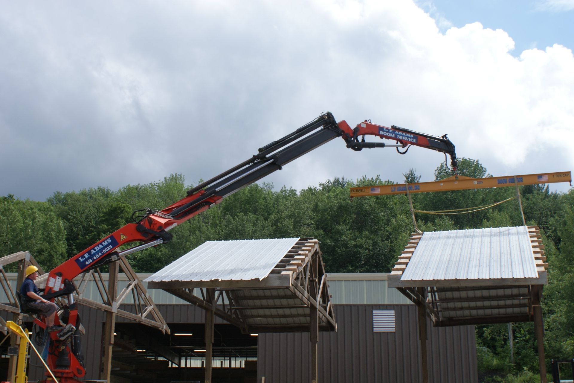 Crane lifting a long beam above a building roof at a construction site under cloudy skies