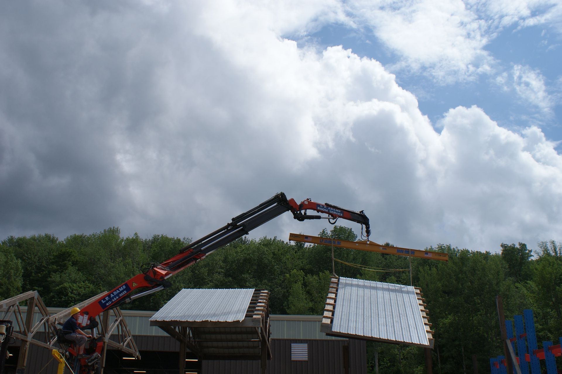 Crane lifting roof panels above a building site under cloudy sky