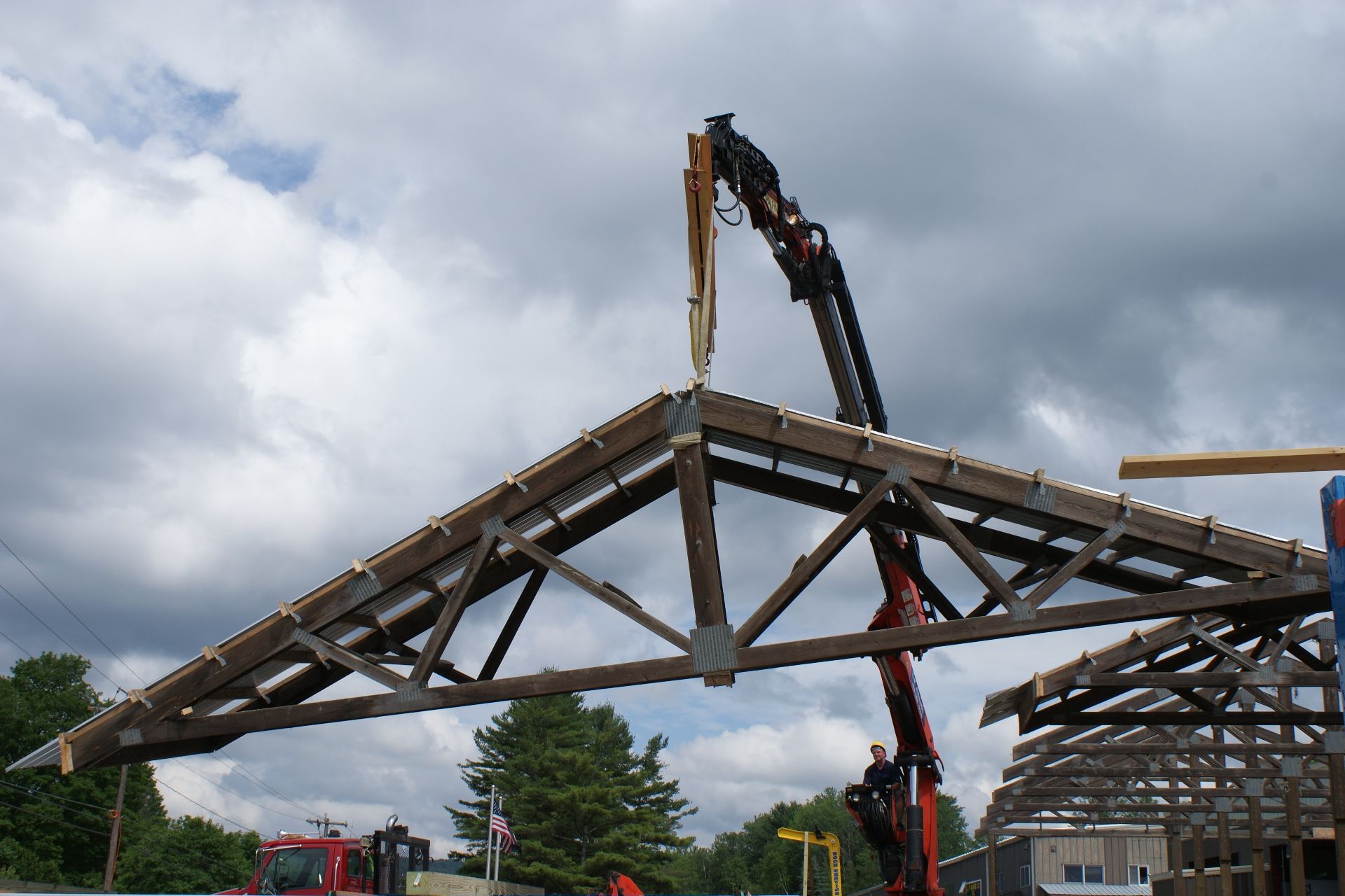 Crane lifting a large wooden truss frame against a cloudy sky at a construction site