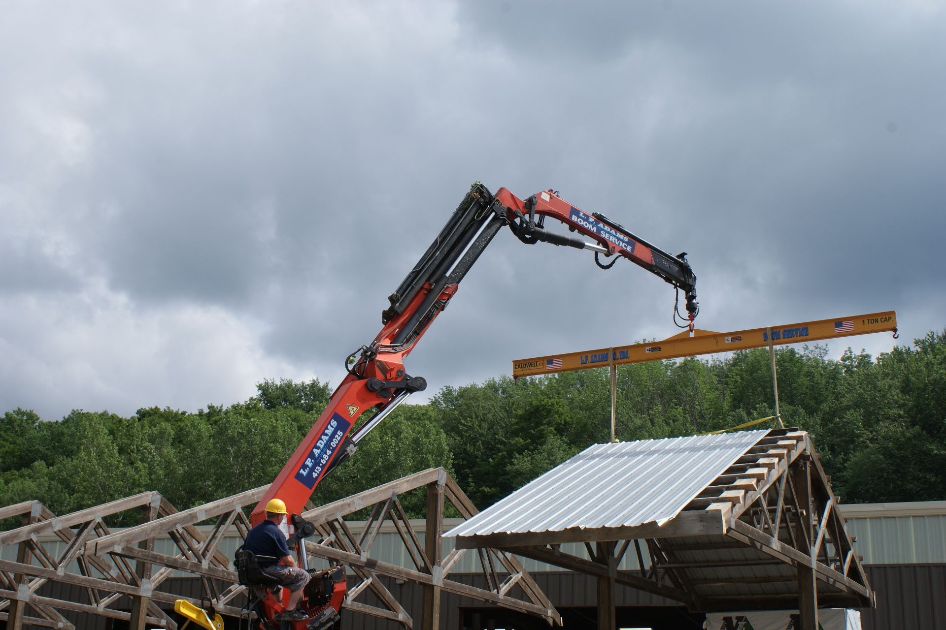Red crane lifting a long wooden beam over a roof under construction in cloudy weather
