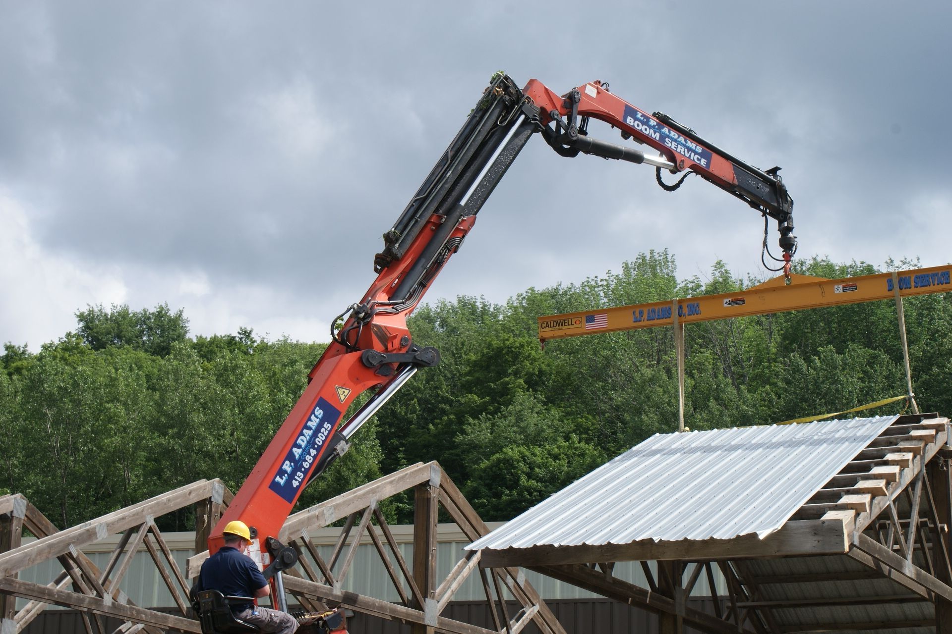 Red crane lifting roof trusses at a construction site under cloudy skies