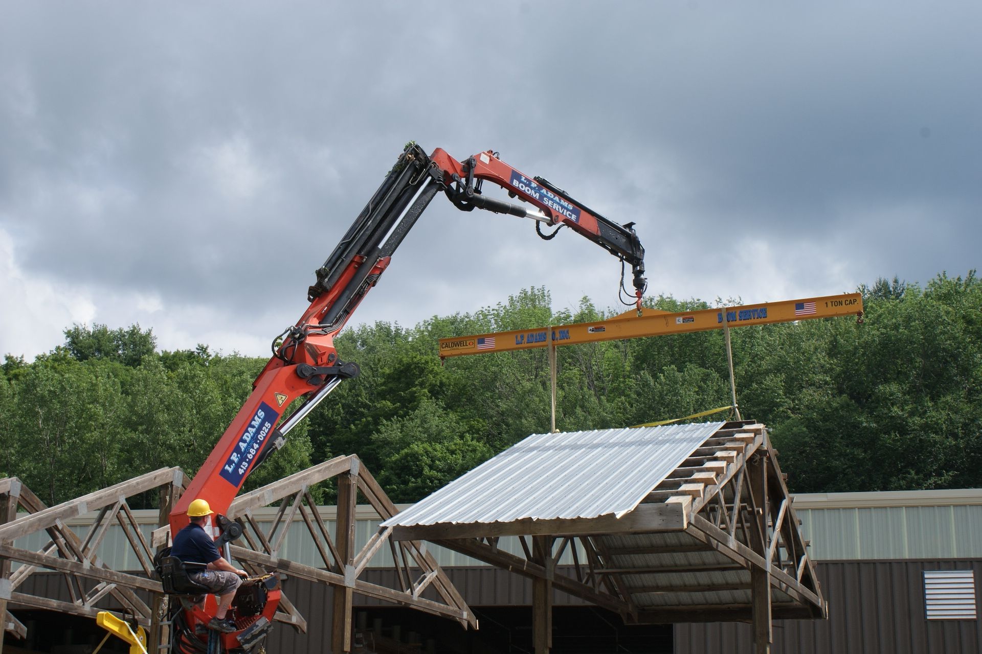 Crane lifting roof trusses at a construction site under cloudy skies.
