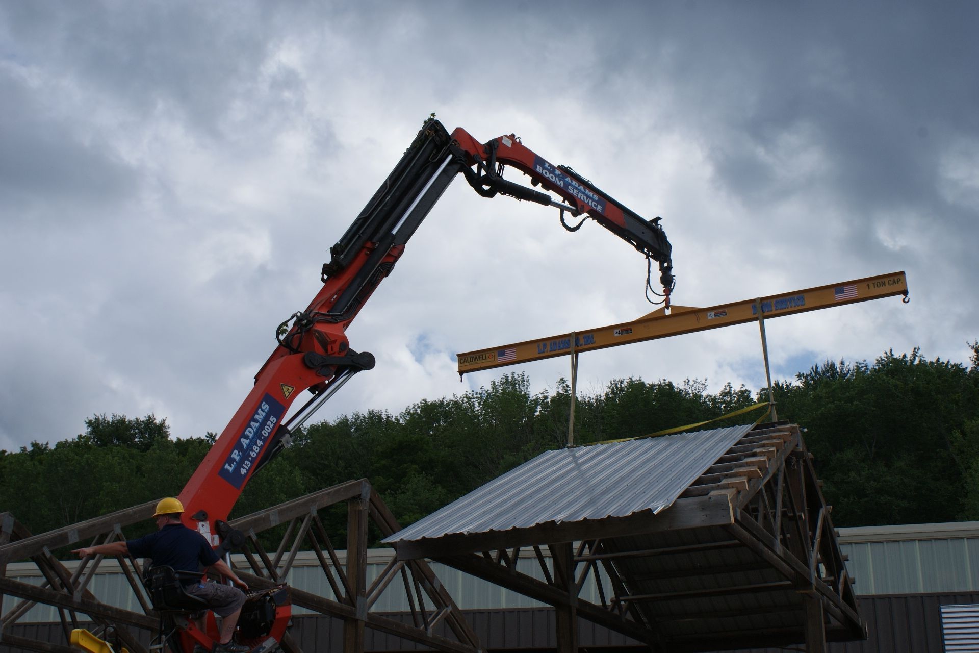 Crane lifting a long wooden beam over a roofless structure under a cloudy sky
