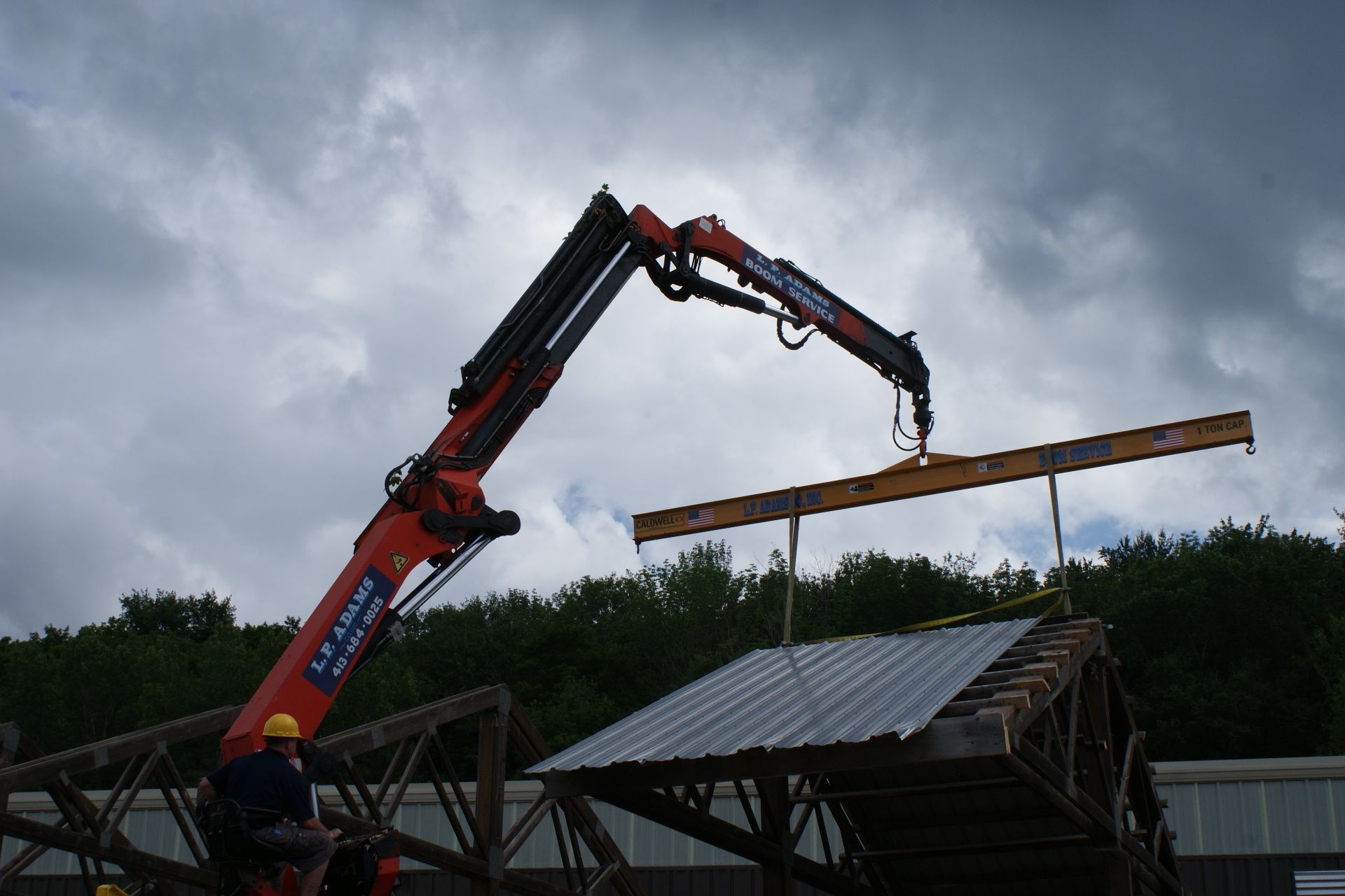 Crane lifting a long beam over a roof under cloudy skies