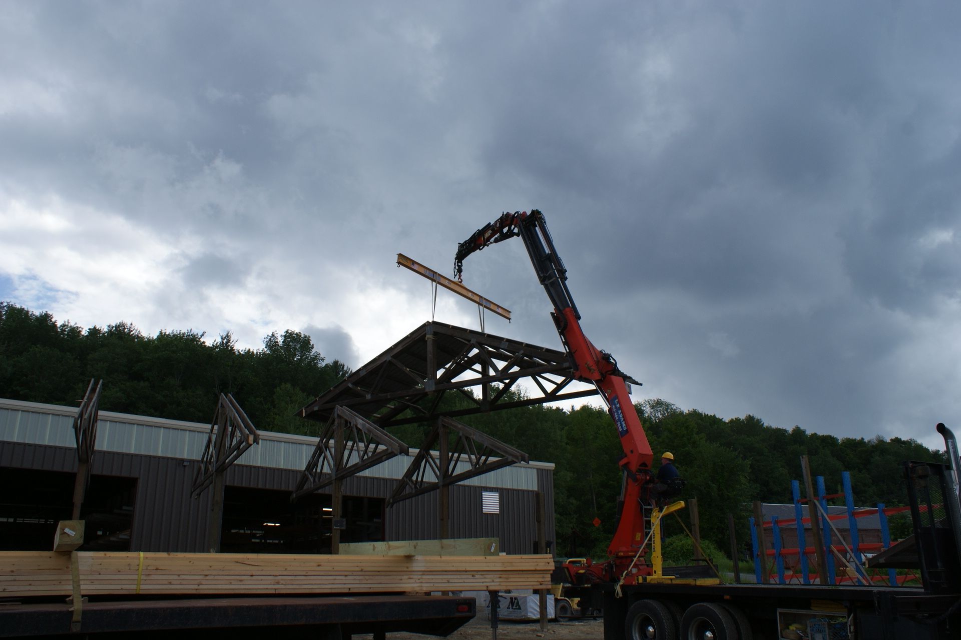 Crane lifting roof beams at a construction site under dark storm clouds