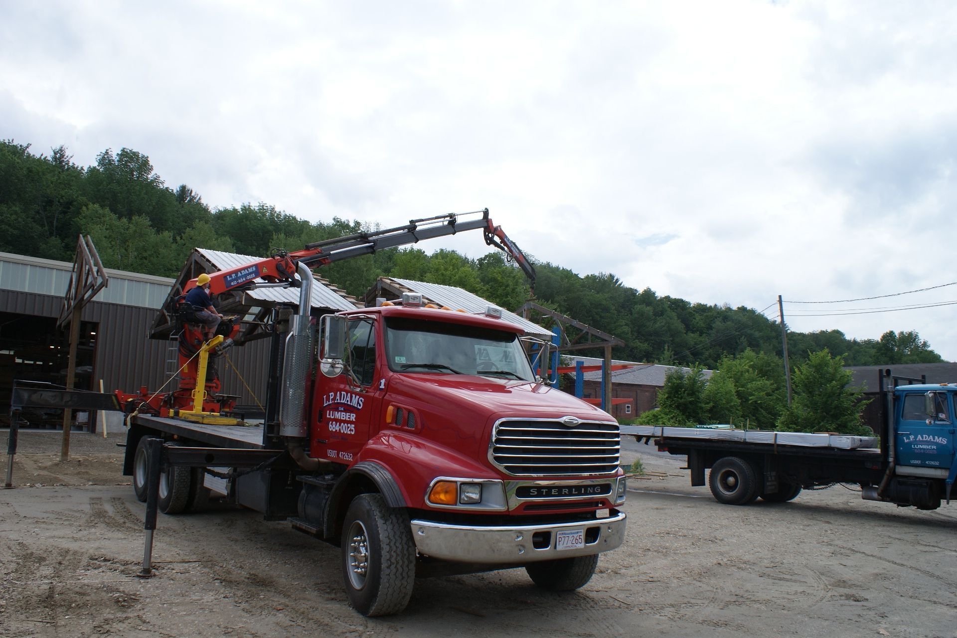 Red tow truck parked on a gravel lot with a blue truck and green hillside in the background