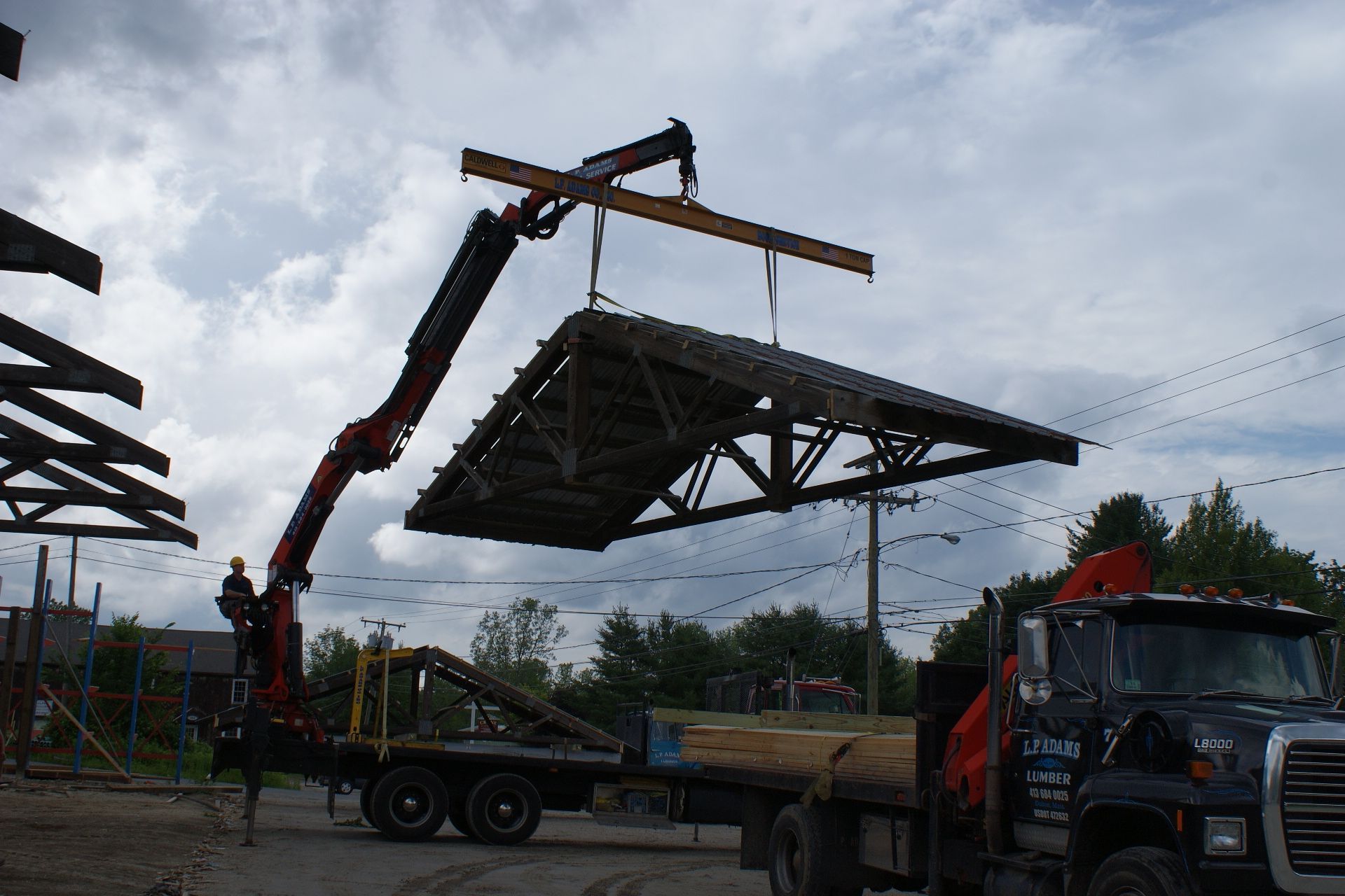 Crane lifting a large metal roof panel onto a truck at an outdoor construction site.