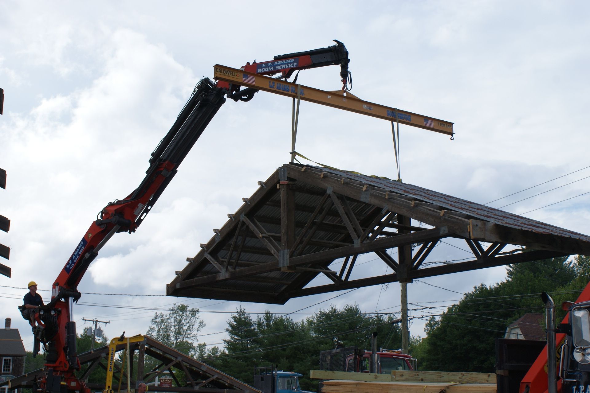 Crane lifting a large triangular roof structure at a construction site under a cloudy sky