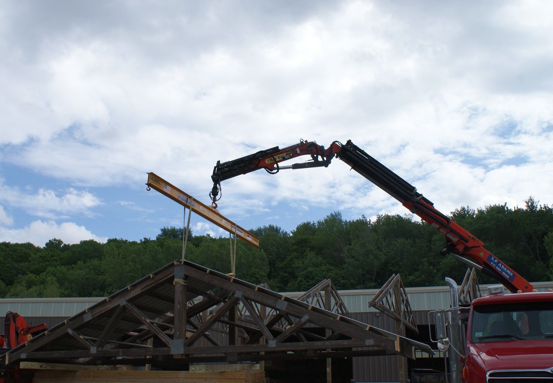 Crane lifting a wooden roof frame at a construction site under a cloudy sky