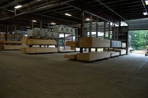 Large warehouse interior with stacked lumber bundles and an open loading area near a bright doorway