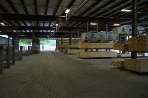 Large warehouse interior with stacked lumber and pallets along a wide concrete aisle