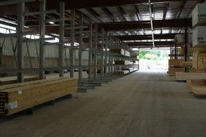 Empty warehouse interior with stacked lumber and shelves, looking toward a bright open doorway