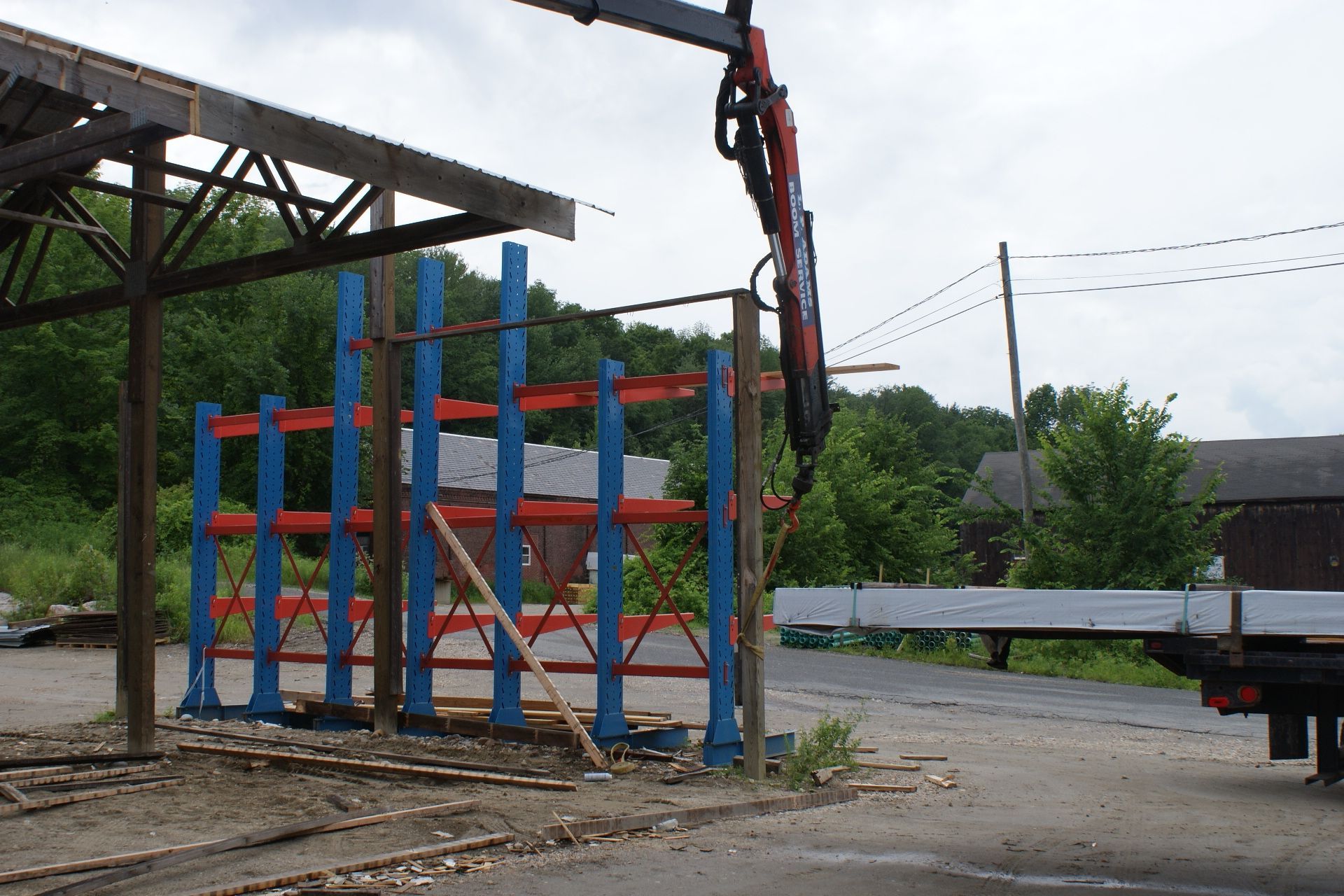 Covered industrial loading area with blue steel rack and a crane arm beside a gravel lot