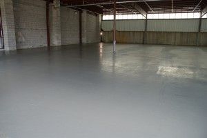 Empty warehouse with a smooth gray concrete floor and corrugated metal walls.