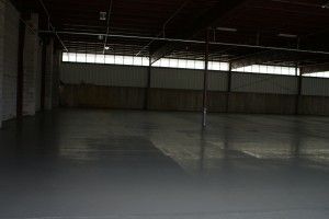 Empty warehouse interior with concrete floor and large windows letting in dim light