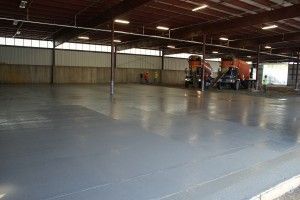 Empty warehouse with a polished concrete floor and two orange forklifts in the back right.