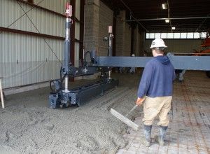 Worker in hard hat guiding a large gray industrial machine inside a warehouse.