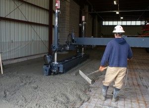 Worker in hard hat guiding a concrete pump inside an industrial building.