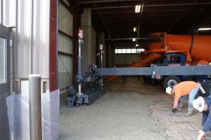 Workers in a warehouse unloading gravel from an orange machine onto the floor