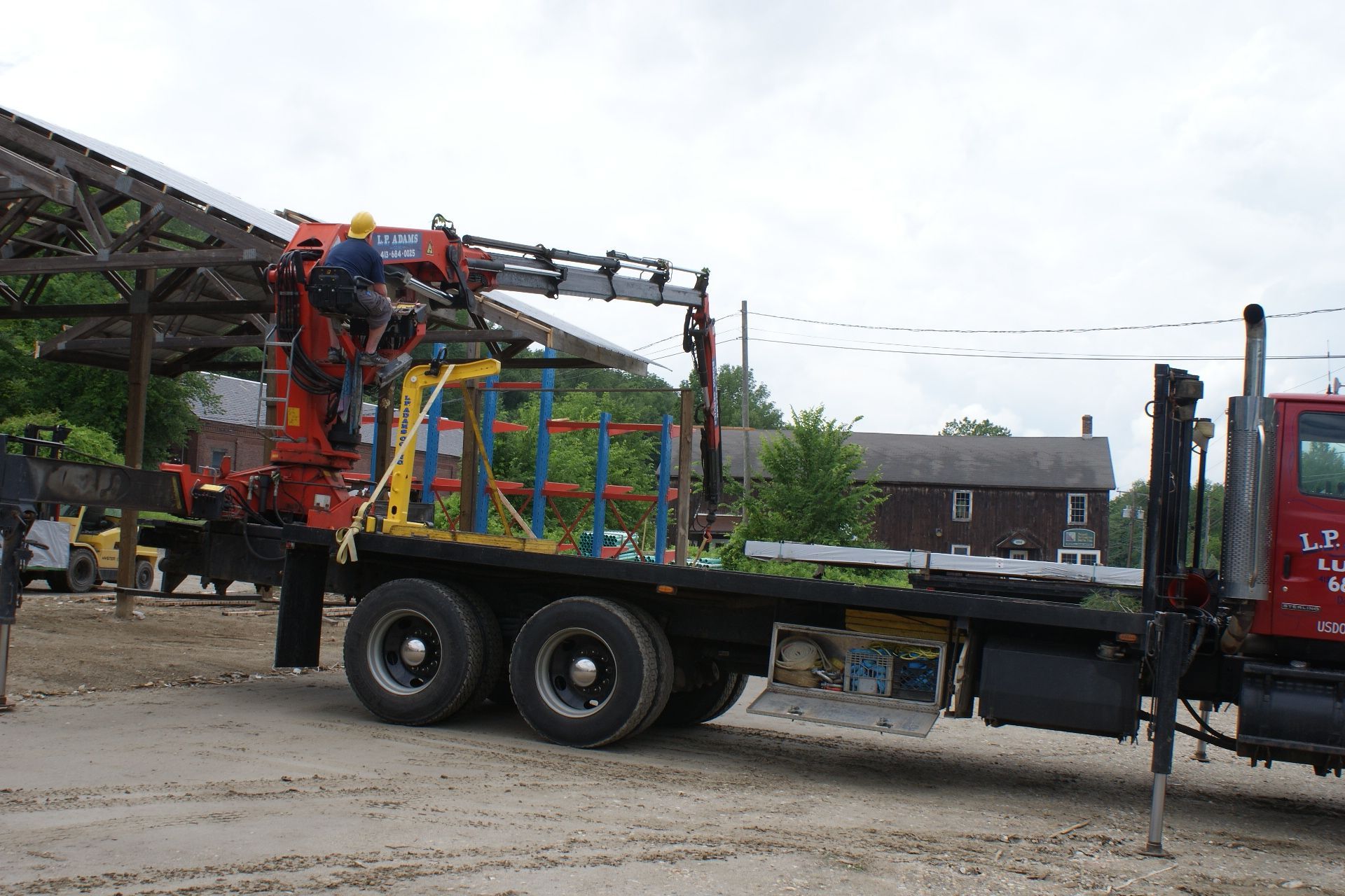 Truck-mounted crane lifting colorful equipment in an industrial yard