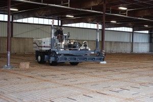 Large farm machine working inside an empty barn with dirt floor and metal walls