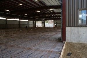 Empty warehouse interior with exposed beams, concrete floor, and daylight through windows