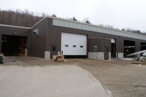 Industrial warehouse with large white loading door and parked car outside on a muddy lot