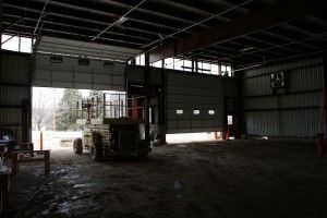 Dim warehouse interior with a forklift near an open loading door and daylight outside.