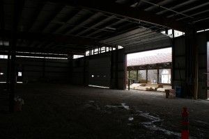 Empty dim warehouse interior with a bright opening and construction materials near the entrance