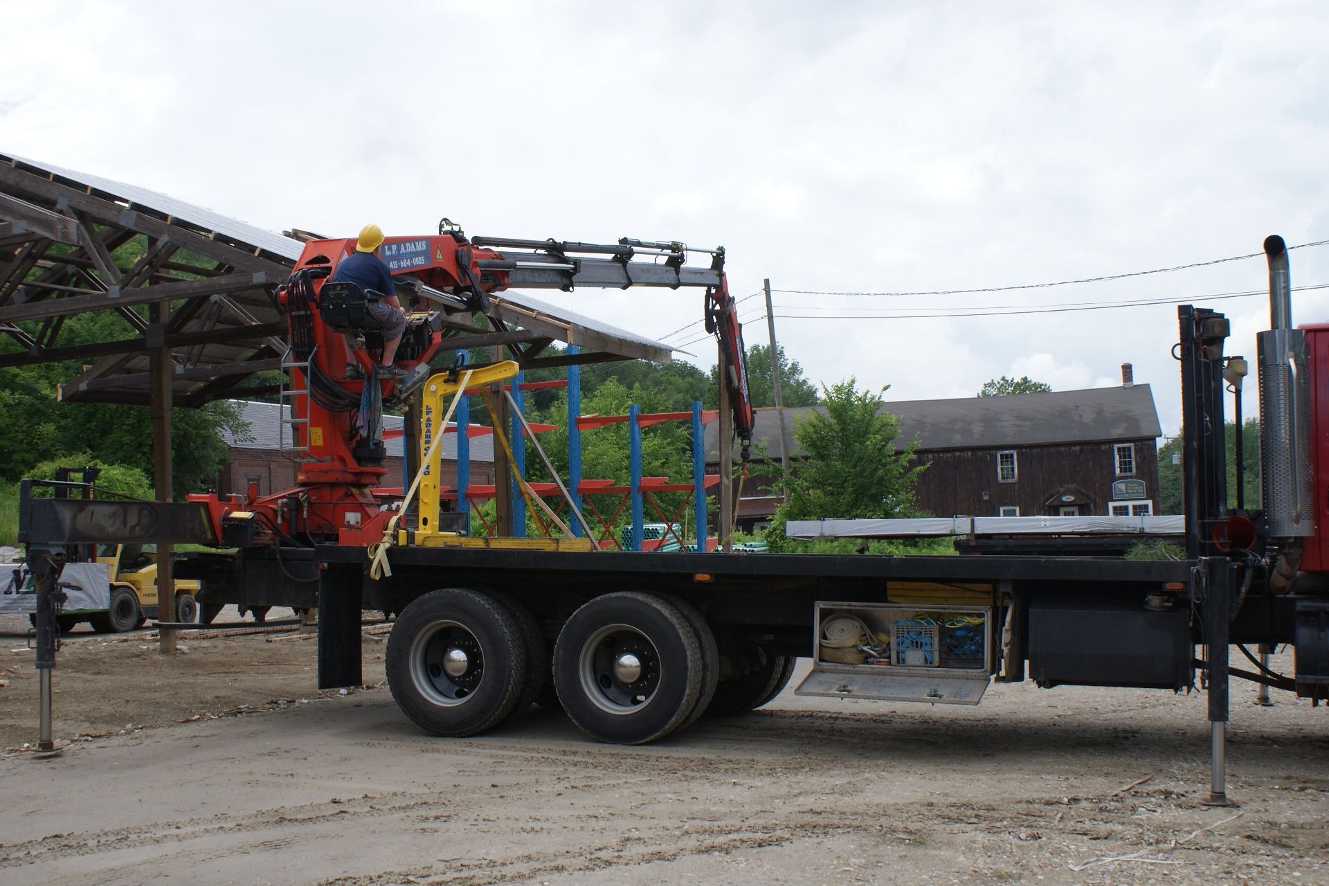 Crane truck loading a colorful structure onto a flatbed in an industrial yard