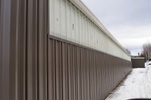 Long metal-sided building beside a snow-covered path on an overcast day