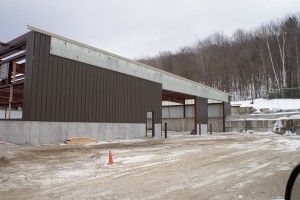 Snowy construction site with a large brown building and a concrete overhang