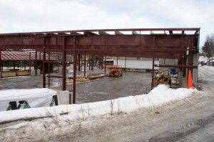 Snowy construction site with steel framework, equipment, and orange cones under an overcast sky