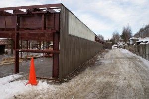 Snowy alley beside long brown shed with an orange traffic cone in front