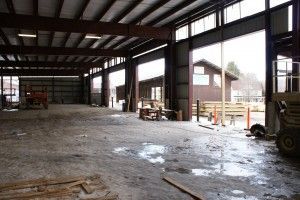 Empty steel warehouse with wet concrete floor and large open bay doors.